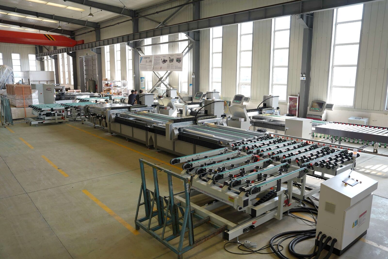 Glass laser drilling line in the workshop, with laser drilling machines, transfer tables and the tilting unloading table next to a glass rack